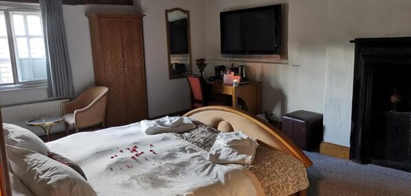 A hotel room with a bed, a chair, a desk, a television, and a fireplace.