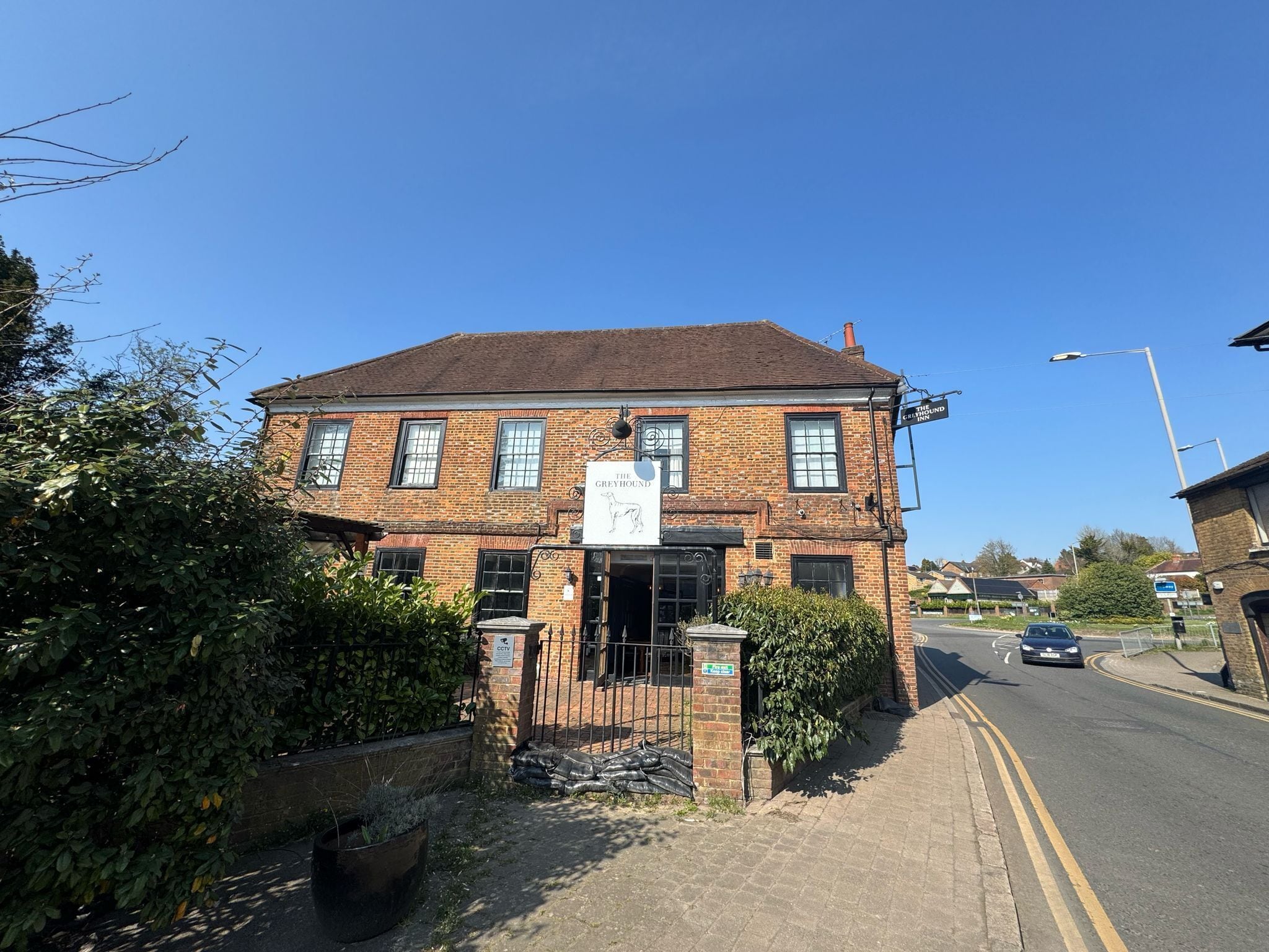 A traditional brick building with a sign for 'The Greyhound Inn' and a gated entrance.