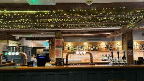 Zona de bar con vigas de madera, luces colgantes y una variedad de botellas y vasos.