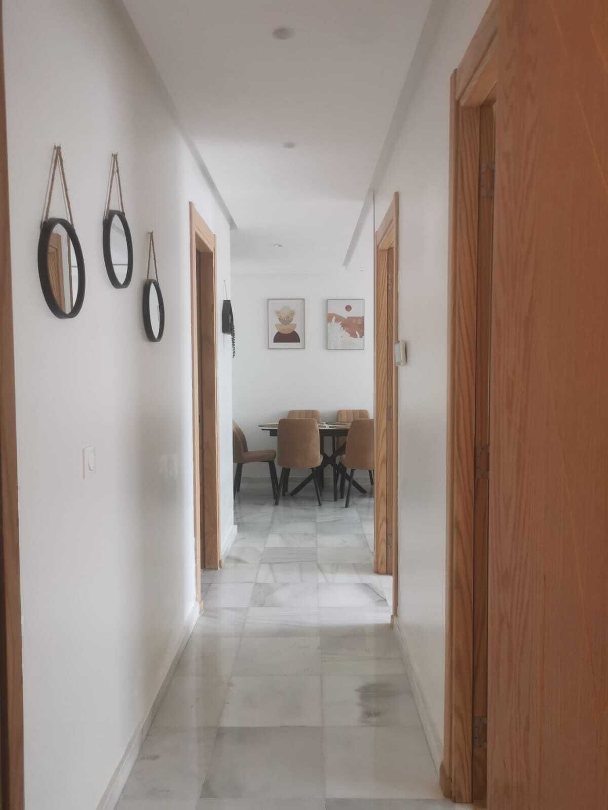 A hallway with a dining area at the end, featuring a table and chairs.