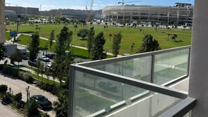 Une vue depuis un balcon donnant sur un chantier de construction, avec un stade et un parking.