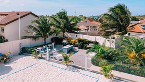 Zona de playa arenosa con piscina, asientos al aire libre y palmeras.