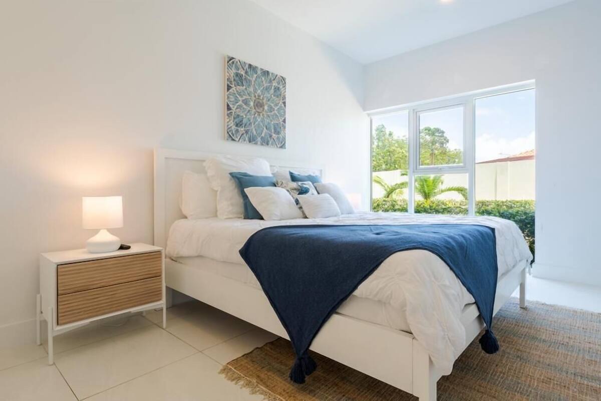 A bedroom with a bed, nightstand, and a window with a view of greenery.