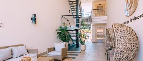 A spacious lobby with a staircase, wicker furniture, and potted plants.