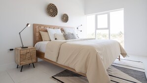 Un dormitorio moderno con una cama de madera, una mesita de noche, un escritorio y un ventanal grande.