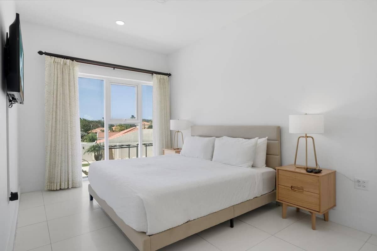 A bedroom with a bed, bedside lamps, a wooden nightstand, and a TV mounted on the wall.