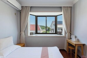 A hotel room with a bed, a desk, and a window with curtains.