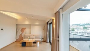 Een moderne woonkamer met een bank, een salontafel en uitzicht op een stadsgezicht door grote ramen.