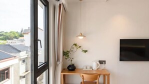 Een kamer met een houten bureau, een potplant, een hanglamp en een televisie aan de muur.