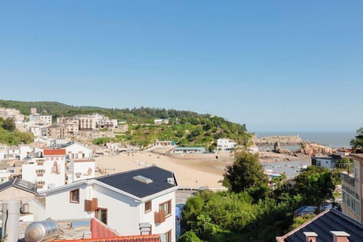 A coastal town with buildings, a beach, and rocky cliffs.