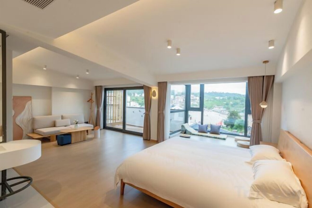 Et moderne hotelværelse med en stor seng, et siddeområde og en balkon med udsigt over byen.
