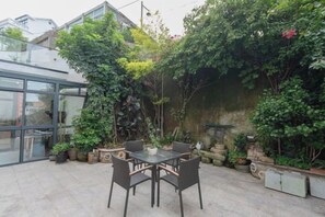An outdoor patio with a table and chairs, surrounded by potted plants and a stone wall.