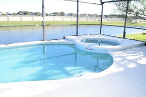 Une piscine avec un jacuzzi, entourée d’une zone abritée et délimitée par une clôture.