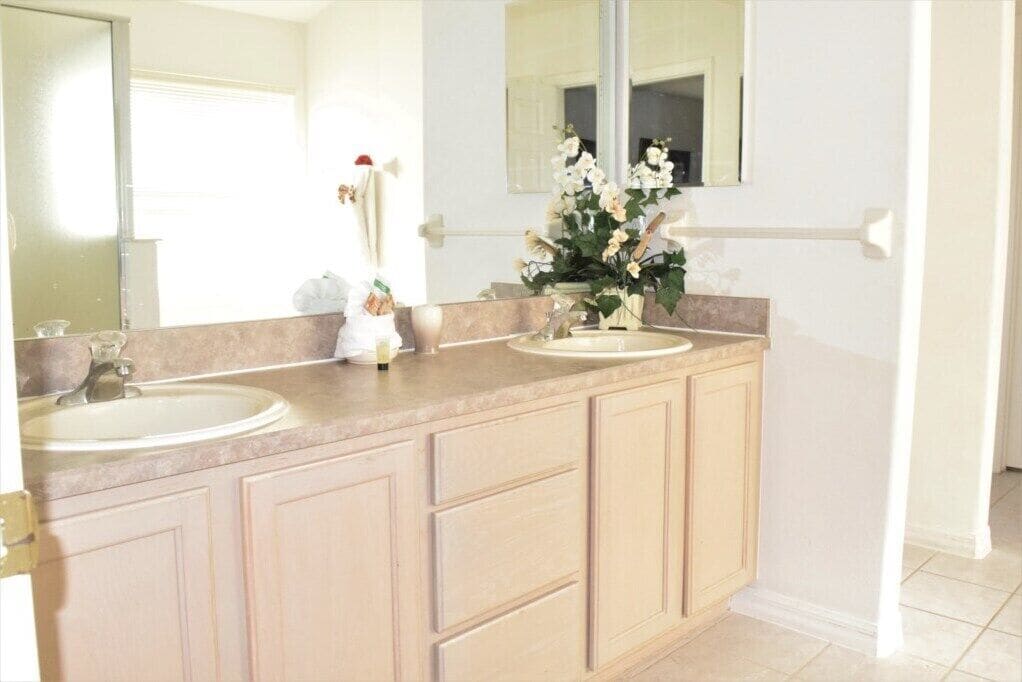 Une salle de bain avec deux lavabos, un grand miroir et un vase rempli de fleurs.