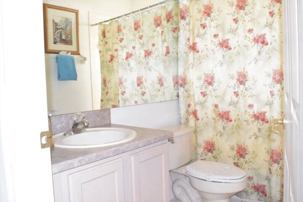 Un bagno con un lavandino bianco, un water e una tenda da doccia con motivo floreale.