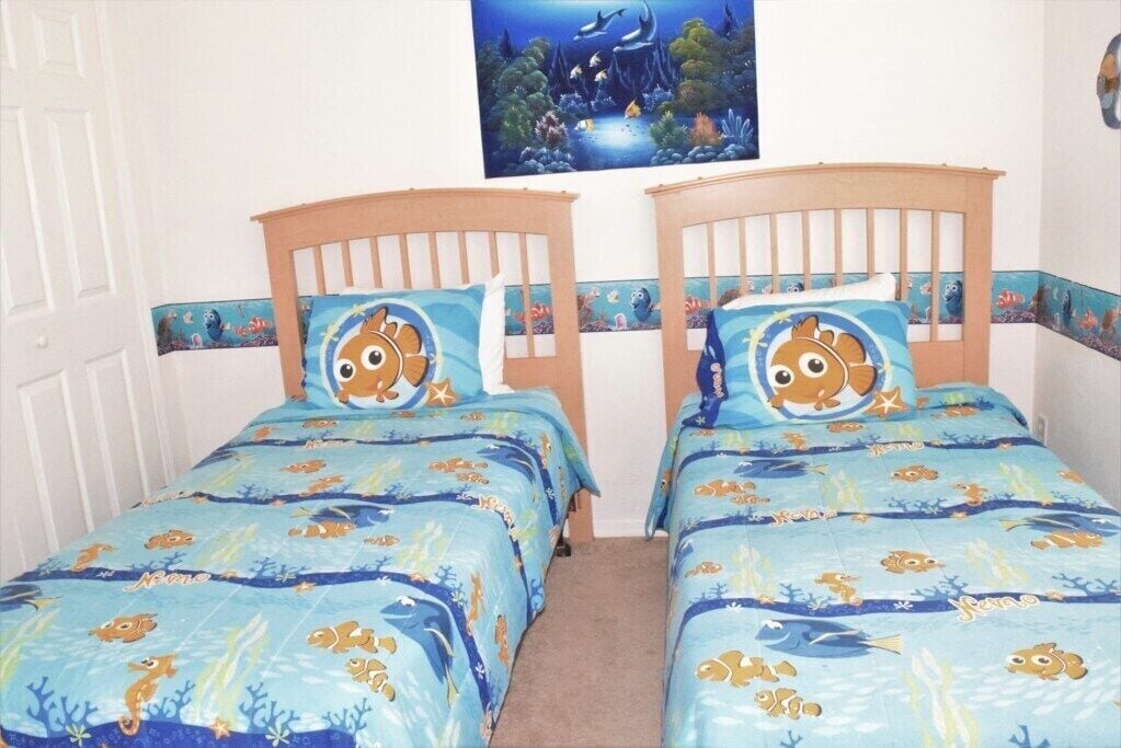 A bedroom with two single beds, each with a blue ocean-themed bedspread and matching pillows.