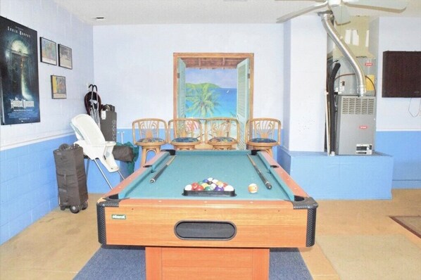 Une table de billard avec des chaises, une affiche, un radiateur et une vue sur l’extérieur.