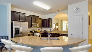 A modern kitchen with dark cabinets, stainless steel appliances, a granite countertop, and a built-in sink. - Villa Du Soleil (Davenport)