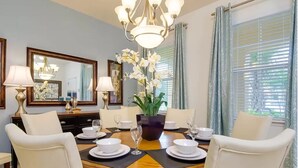 A dining room with a round table set for four, surrounded by white chairs. There is a chandelier above the table, and a large mirror on the wall. - Villa Du Soleil (Davenport)