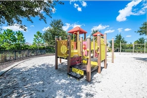 Ein Spielplatz mit Klettergerüsten und Rutschen, umgeben von Sand und einem Zaun.
