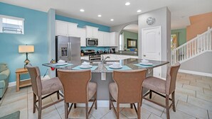 A modern kitchen with white cabinets, a central island with bar stools, and a stainless steel refrigerator. - 5419 Oakgrain (Davenport)