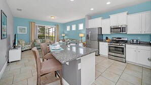 A modern kitchen with white cabinets, a granite countertop, stainless steel appliances, and a dining area with a table and chairs. - 5419 Oakgrain (Davenport)