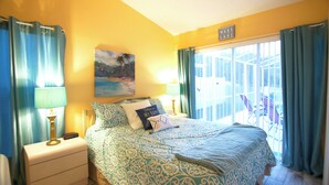 A bedroom with a bed, two bedside tables, a painting, and a view of the outside. - Hummingbird Haven (Davenport)