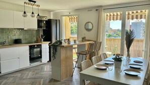 Een moderne keuken met witte kasten, een centraal eiland en een eethoek met rieten stoelen.