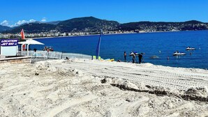 Een strand met een jetski-verhuurzone, een zandige voorgrond en een helderblauwe lucht.