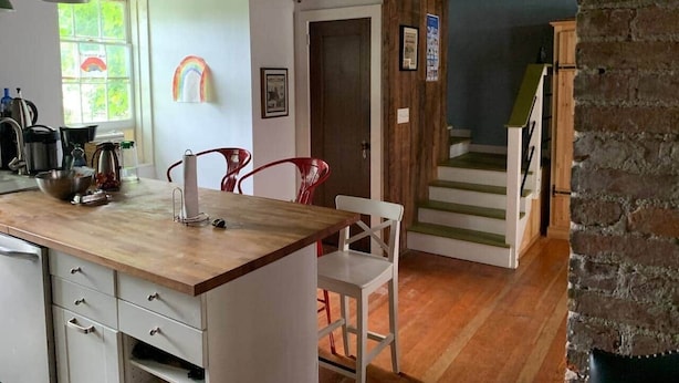 Cocina con encimera de madera, armarios blancos y sillas rojas. Una escalera conduce a otra habitación.