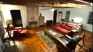 Un loft espacioso con techos altos, vigas de madera a la vista y una amplia sala de estar con un sofá rojo, una mesa de centro de madera y una chimenea.