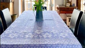 Comedor con una mesa cubierta con un mantel estampado, un florero con flores y un ventilador de techo.