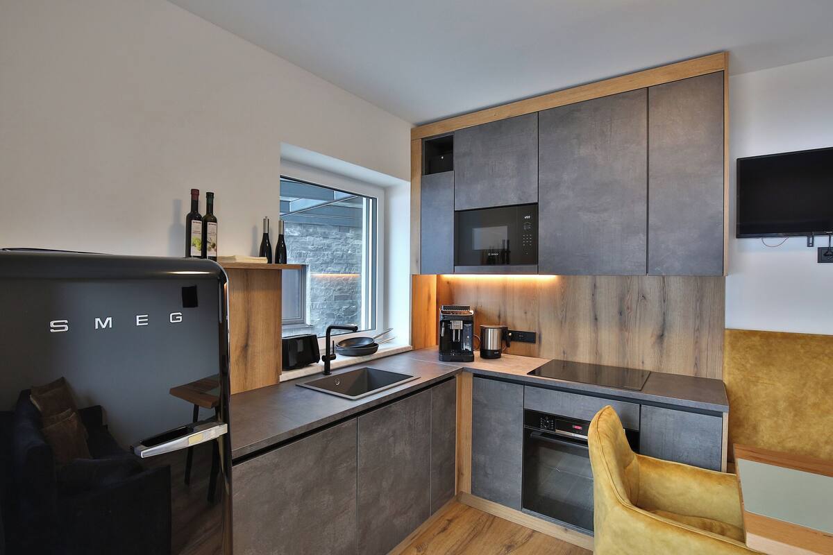 A modern kitchen with a built-in oven, a coffee machine, and a wine bottle on the counter.