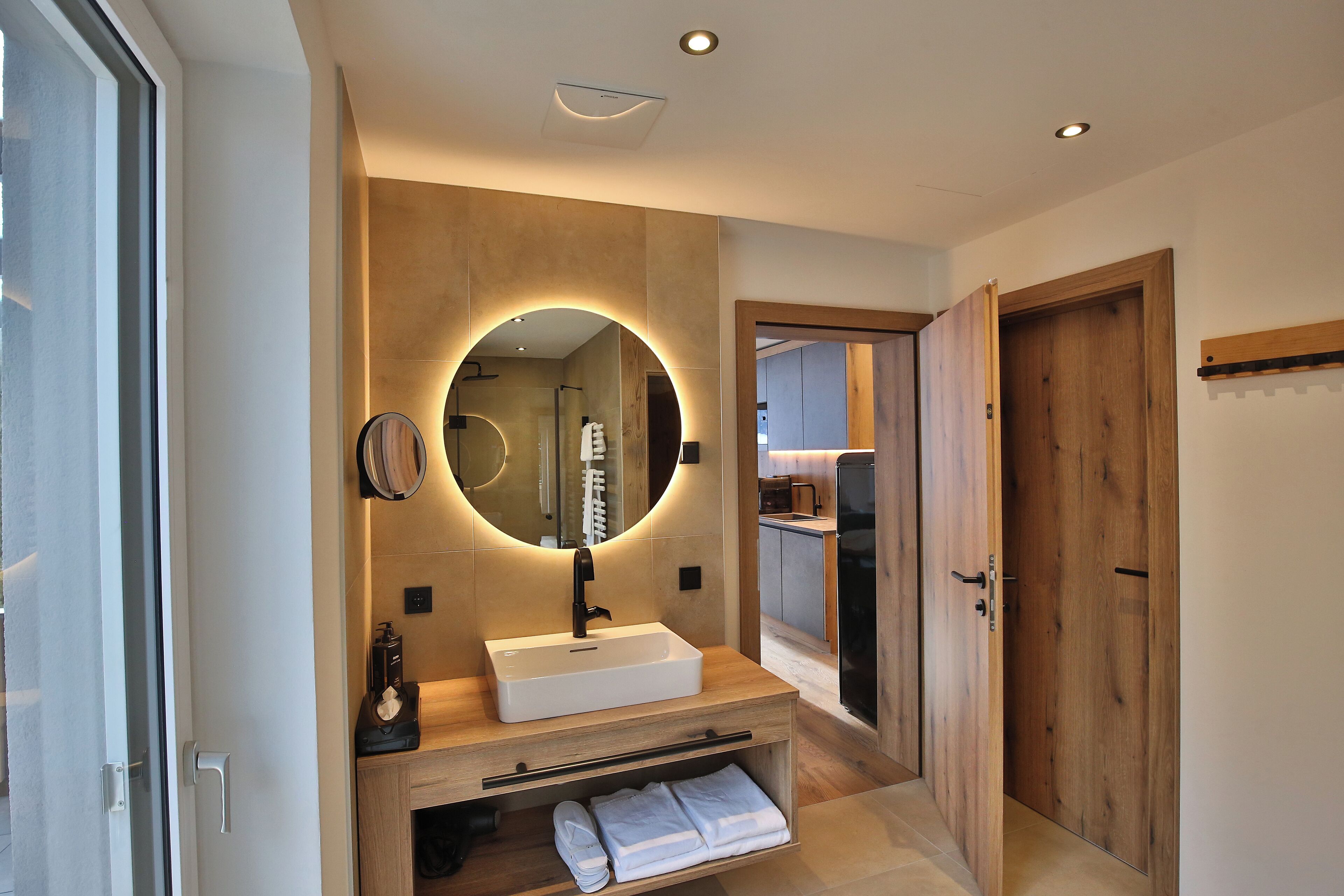 A modern bathroom with a large mirror, a white sink, and a wooden vanity.