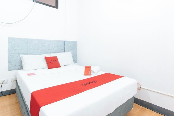A hotel room with a bed, a red and white bedspread, and a white pillow.