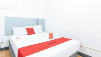A hotel room with a bed, a red and white bedspread, and a white pillow.