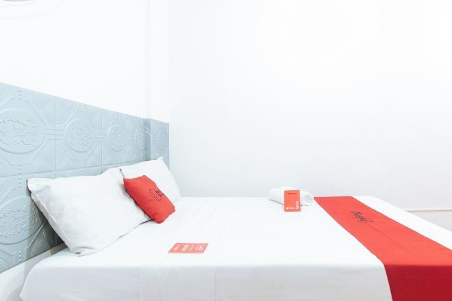 A hotel room with a bed, pillows, a red and white bedspread, and a wall with a geometric pattern.
