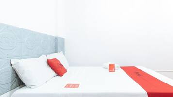 A hotel room with a bed, pillows, a red and white bedspread, and a wall with a geometric pattern.