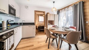 A modern kitchen with a dining area, wooden flooring, and a view of a bedroom.