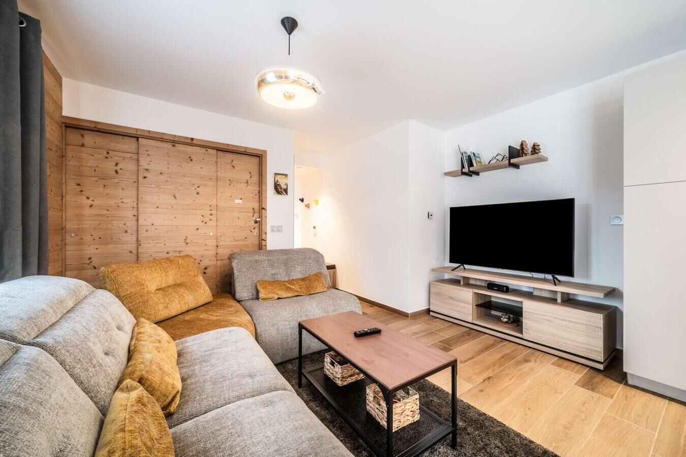 Een moderne woonkamer met een modulaire bank, een salontafel, een televisie en een houten garderobe.
