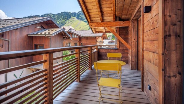A wooden balcony with a metal railing, a yellow chair, and a small table.