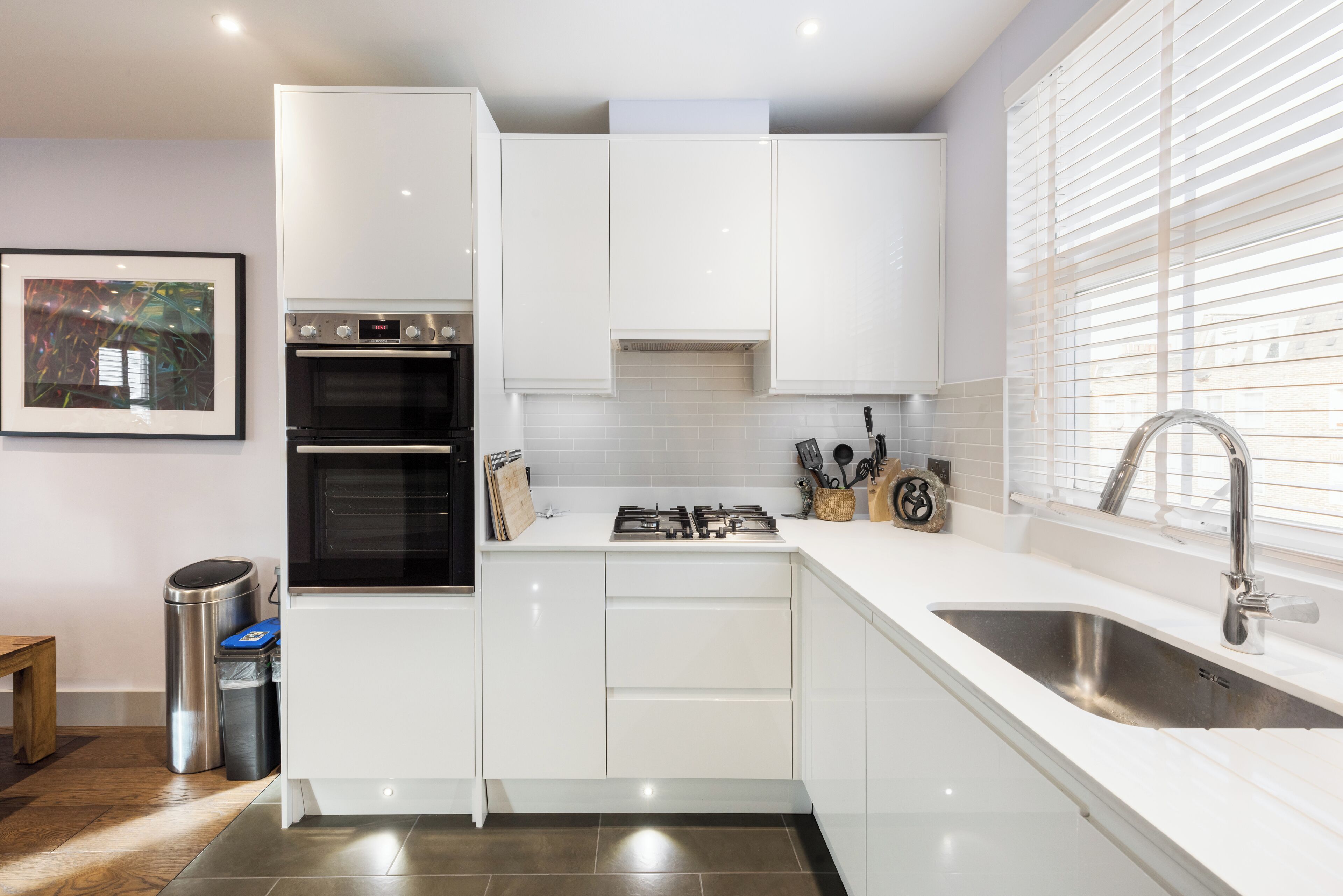 Una cucina moderna con mobili bianchi, forno integrato, piano cottura a gas e lavello in acciaio inossidabile.