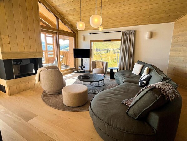 A modern living room with a fireplace, comfortable seating, and large windows offering a view of the outdoors.
