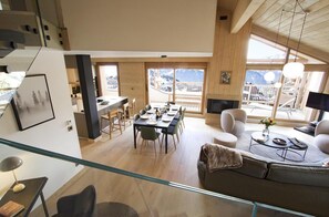 A modern living room with a glass staircase, a dining area with a wooden table and chairs, and a sofa with a coffee table.