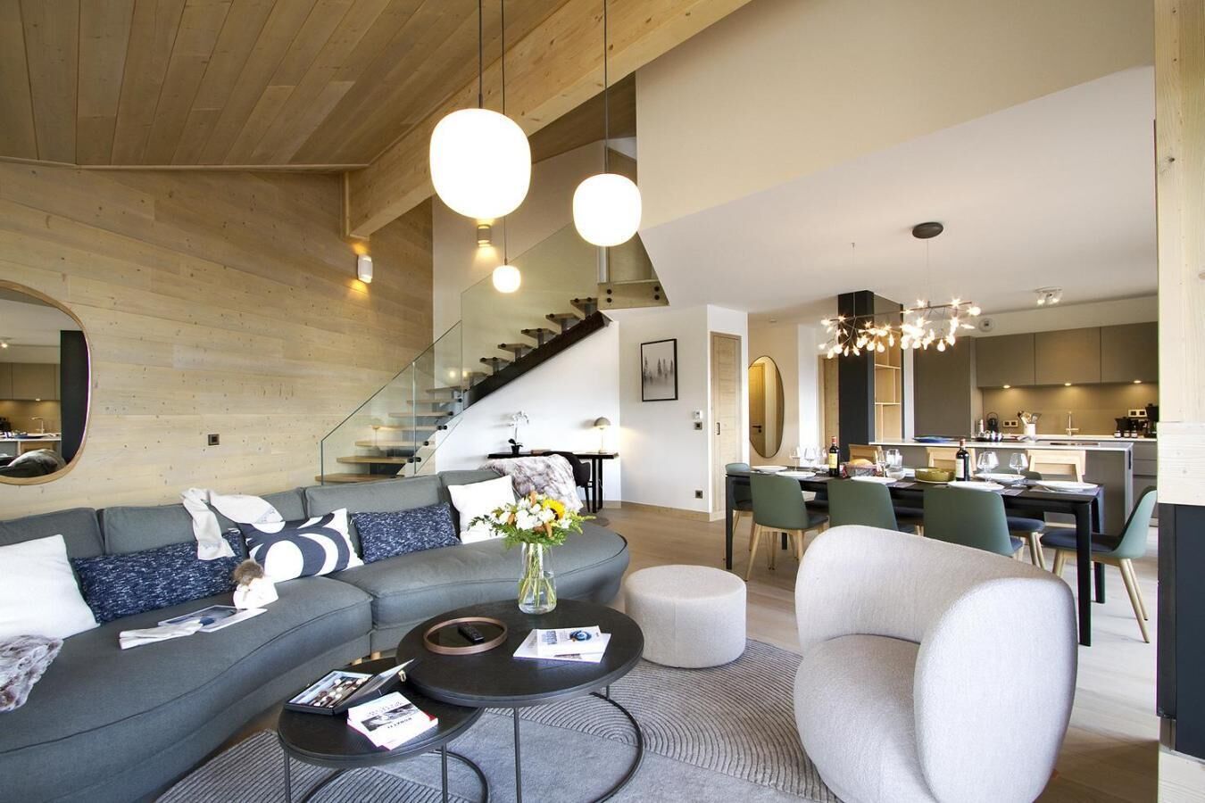 A modern living room with a grey sofa, a round coffee table, and a dining area with a chandelier.