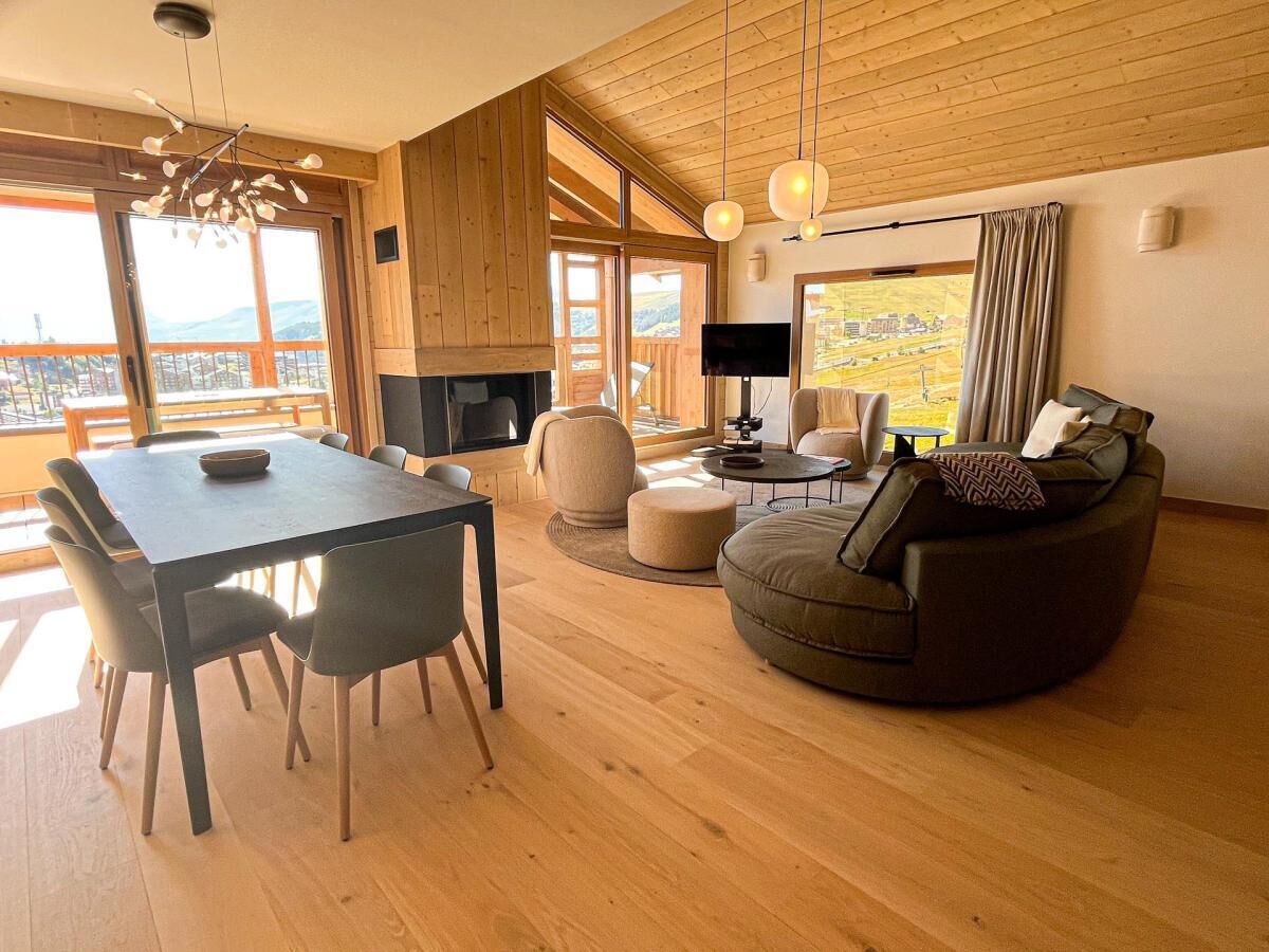 A modern living room with a wooden floor, a round sofa, a dining table with chairs, and a fireplace.