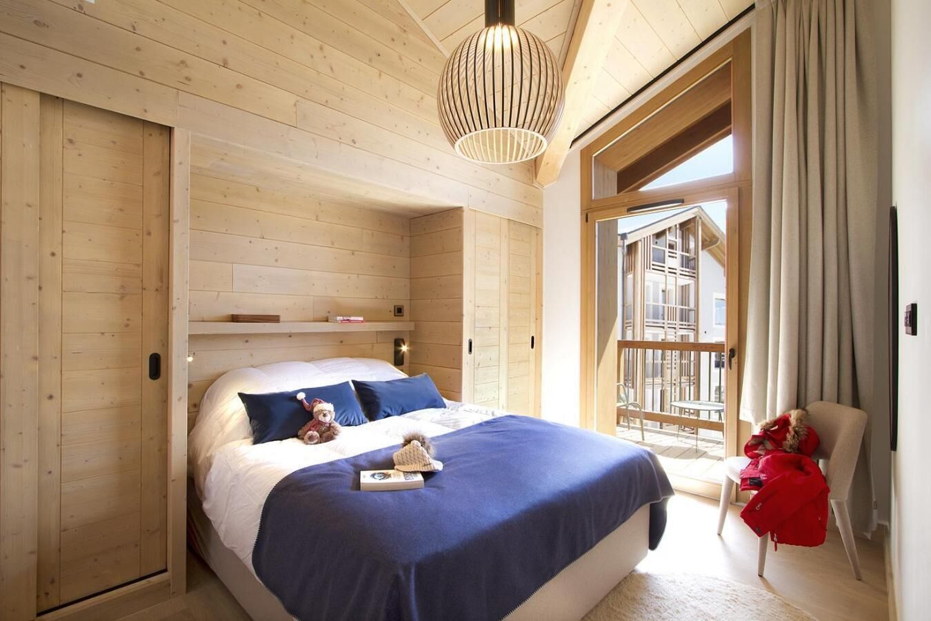 Ein Zimmer mit Holzboden, einem Bett, einer Pendelleuchte und Blick ins Freie.