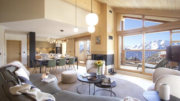 Ein modernes Wohnzimmer mit großem Fenster und Blick auf die Berge, einer gemütlichen Sitzecke sowie einem Essbereich mit Küche im Hintergrund.
