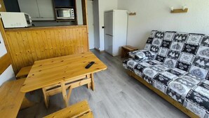 A compact room with a wooden table and benches, a patterned sofa, a microwave, and a refrigerator.