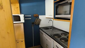 A compact kitchen with a microwave, stove, sink, and wooden cabinets.
